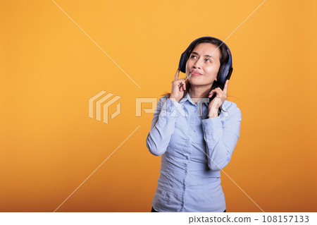 Smiling joyful woman with headphones listening music, dancing in studio over yellow background. Filipono model having fun, showing dance moves during break time. Entertainment concept Smiling joyful woman with headphones listening music, dancing in studio over yellow background. Filipono model having fun, showing dance moves during break time. Entertainment concept 108157133