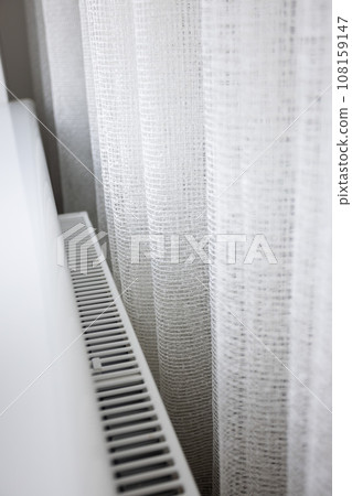 Modern radiator behind the curtains at home. Central heating system 108159147