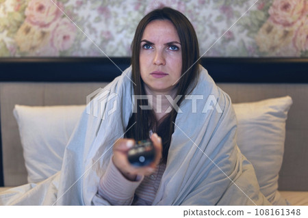 A woman suffering from insomnia, sits on the bed switches channels on the TV 108161348
