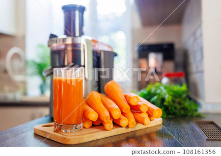 Glass of freshly squeezed carrot juice, carrots and juicer in the kitchen 108161356