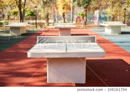 Table tennis tables in autumn public park. Concrete tennis table in a city park ping pong game Table tennis tables in autumn public park. Concrete tennis table in a city park ping pong game 108161704