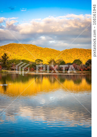 In autumn at Daikakuji Monzeki, the water mirror of Osawa Pond reflects the mountains of Sagano, where the autumn leaves shine golden in the setting sun. 108161948