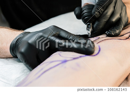 Professional tattoo artist makes a tattoo on the male leg 108162143