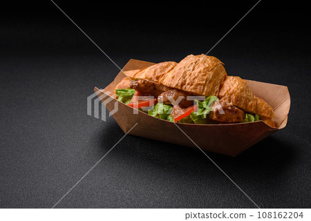 Delicious fresh crispy croissant with chicken or beef meat, lettuce, tomatoes, spices and sauce 108162204