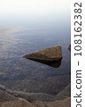 Rocks by the water and clouds reflected on the water surface 108162382