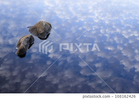 Stones by the water and clouds reflected on the water surface 108162426