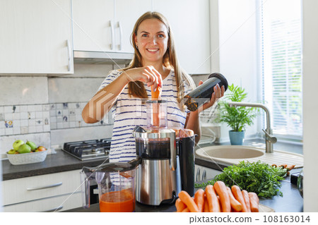 A woman making carrot juice from fresh carrots with a home juicer in the kitchen A woman making carrot juice from fresh carrots with a home juicer in the kitchen 108163014
