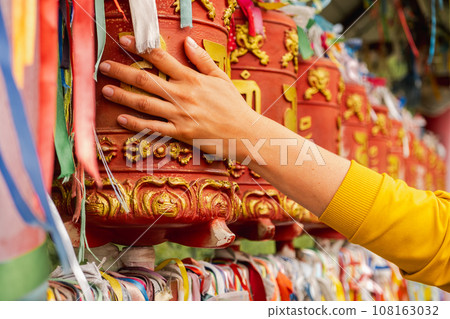 Person pilgrim female hand touching turning spinning Buddhist prayer wheel at Buddhist monastery. Prayer wheels in Buddhist stupa temple. Buddhism religion concept 108163032