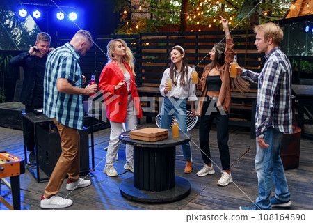 Group of young cheerful friends are enjoying a time together at a barbecue party in the cozy evening garden. Group of young cheerful friends are enjoying a time together at a barbecue party in the cozy evening garden. 108164890