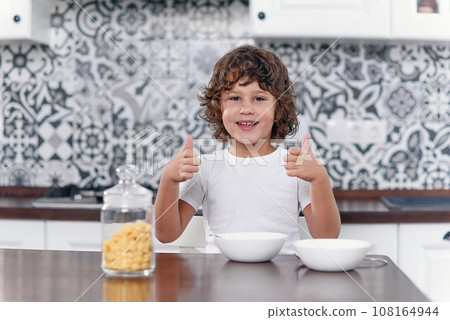 Happy boy feels happiness while eating healthy breakfast of cornflakes and milk at the kitchen. Happy boy feels happiness while eating healthy breakfast of cornflakes and milk at the kitchen. 108164944