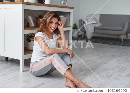 Attravtive smiling girl sits on the floor at the modern kitchen. Womens housework concept. Stay at home wife. Attravtive smiling girl sits on the floor at the modern kitchen. Womens housework concept. Stay at home wife. 108164990