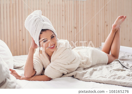 A beautiful happy young woman lies on the bed at home with white cover magazine near her. Beautiful girl enjoying on the bed in morning. 108165276