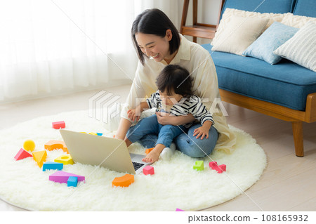 A mother looking at a computer while holding her child A mother looking at a computer while holding her child 108165932