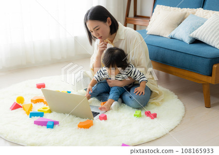 A mother looking at a computer while holding her child 108165933
