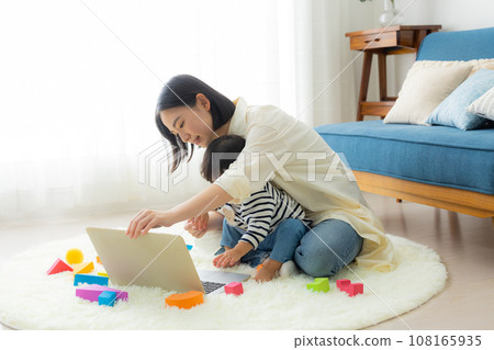 A mother looking at a computer while holding her child 108165935