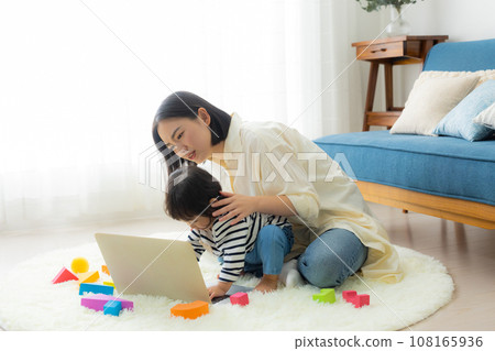A mother looking at a computer while holding her child 108165936