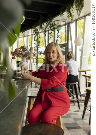 Beautiful Blonde Mature Sexagenarian Woman Drinks Coffee, Tea at Cafe or Restaurant. Modern Senior Female in her 60s wears Red Fashionable Suit, Enjoys Her Life, Time. Happy Retirement. Vertical Beautiful Blonde Mature Sexagenarian Woman Drinks Coffee, Tea at Cafe or Restaurant. Modern Senior Female in her 60s wears Red Fashionable Suit, Enjoys Her Life, Time. Happy Retirement. Vertical 108166117