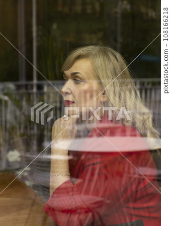 Portrait Beautiful Blonde Mature Sexagenarian Woman Sitting Behind Window Glass of Restaurant or Cafe. Stylish Modern Senior Female in her 60s Thinking About Something. Retirement. Vertical Plane Portrait Beautiful Blonde Mature Sexagenarian Woman Sitting Behind Window Glass of Restaurant or Cafe. Stylish Modern Senior Female in her 60s Thinking About Something. Retirement. Vertical Plane 108166218