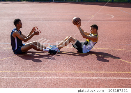 Men basketball players sitting together on court throwing ball to each other. 108167231