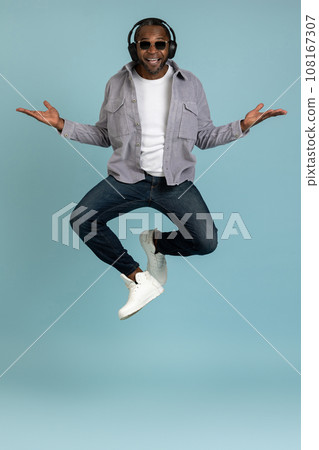 Bearded dark skinned man in headphones dancing making movements to music jumping copy space Bearded dark skinned man in headphones dancing making movements to music jumping copy space 108167307