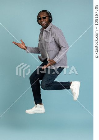 Carefree guy listens lively music modern stereo headphones jumping up to air with happy face Carefree guy listens lively music modern stereo headphones jumping up to air with happy face 108167308