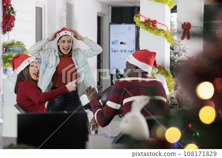 Coworkers having fun in festive decorated office, making fun of each other at work during winter holiday season. Employees laughing together in Christmas ornate workspace Coworkers having fun in festive decorated office, making fun of each other at work during winter holiday season. Employees laughing together in Christmas ornate workspace 108171829