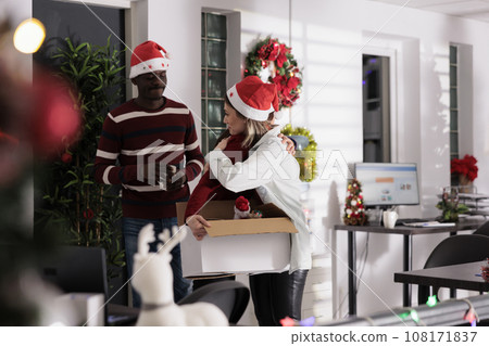 Sad employee packing desk belongings after being discharged on Christmas season, saying goodbye to coworkers. Woman receiving farewell wishes from colleagues after being fired during staff layoffs 108171837