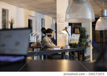 Manager analyzing company investment profit progress report, typing marketing strategy on computer. African american employee working overtime at financial project. Business concept 108171855
