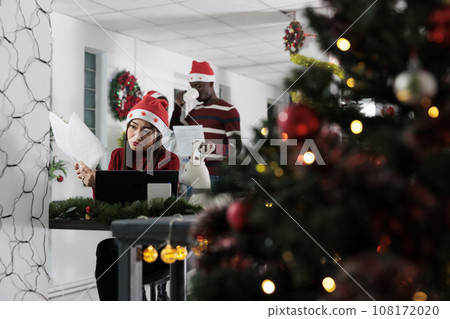 Tired asian employee crosschecking company paperwork in Christmas decorated office. Stressed businesswoman struggling to finish project on time in festive adorn workspace Tired asian employee crosschecking company paperwork in Christmas decorated office. Stressed businesswoman struggling to finish project on time in festive adorn workspace 108172020