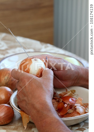 Man's hands peeling freh raw onion with kitchen knife on the kitchen table Man's hands peeling freh raw onion with kitchen knife on the kitchen table 108174139