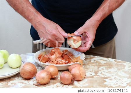 Man's hands peeling freh raw onion with kitchen knife on the kitchen table 108174141