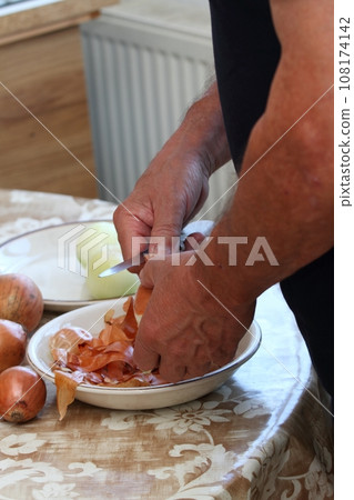 Man's hands peeling freh raw onion with kitchen knife on the kitchen table 108174142