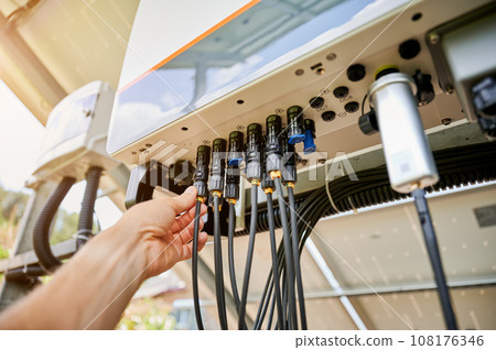Professional worker connecting wires to solar inverter. Pov of configuring inverter. Male worker turning on PV battery. 108176346