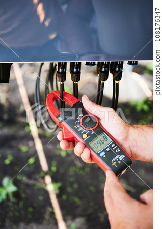 Checking of output voltage level of inverter. Professional worker using current clamps to measure voltage. Techinician service of phototvoltaic battery. Checking of output voltage level of inverter. Professional worker using current clamps to measure voltage. Techinician service of phototvoltaic battery. 108176347