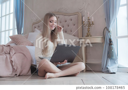Happy young adult woman model with healthy blonde hair sitting on wooden floor in bedroom 108178465