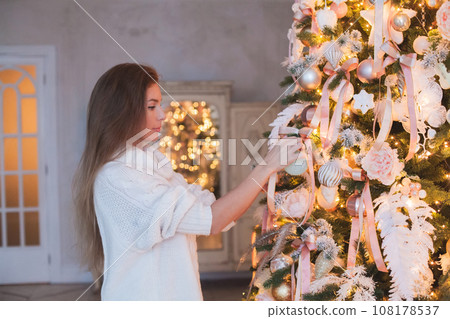 Pretty brunette woman with Xmas tree and Christmas decoration at home Pretty brunette woman with Xmas tree and Christmas decoration at home 108178537
