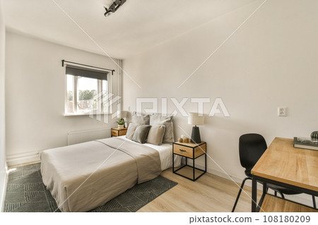 a bedroom with a bed, desk and lamp on the wall in front of the window looking out onto the street 108180209