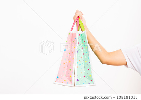 Closeup women hand holding colorful multicolor shopping bag many packets isolated on white background, female holds in hand white clear empty blank craft paper gift bag, shopping day concept Closeup women hand holding colorful multicolor shopping bag many packets isolated on white background, female holds in hand white clear empty blank craft paper gift bag, shopping day concept 108181013