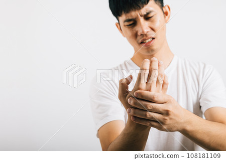 An Asian man, in pain, massages his painful hands and palms. Portrait in a studio shot isolated on white background, highlighting health care and the concept of arthritis. An Asian man, in pain, massages his painful hands and palms. Portrait in a studio shot isolated on white background, highlighting health care and the concept of arthritis. 108181109