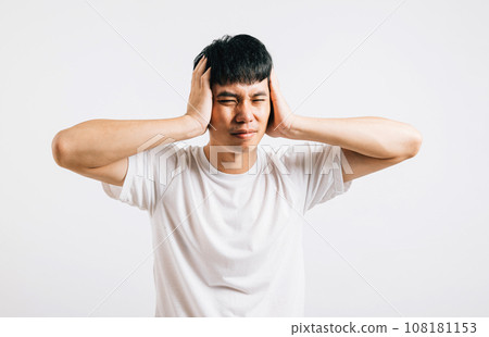 Portrait of a young man in a bad mood, covering his ears with his palms to block out loud noise. Studio shot isolated on white, showcasing his dramatic response to the sound. Portrait of a young man in a bad mood, covering his ears with his palms to block out loud noise. Studio shot isolated on white, showcasing his dramatic response to the sound. 108181153
