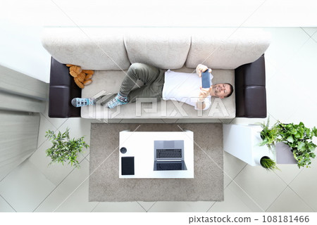 Man lie on sofa and hold modern smartphone in hand Man lie on sofa and hold modern smartphone in hand 108181466