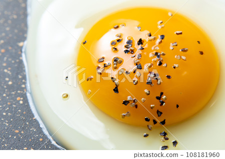 A close-up of the cooking scene of frying a fried egg in a frying pan. (with coarsely ground black pepper) 108181960