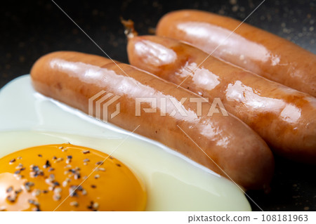A close-up of a cooking scene in which sausages and fried eggs are fried in a frying pan. A close-up of a cooking scene in which sausages and fried eggs are fried in a frying pan. 108181963