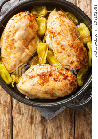Tasty baked chicken fillet with peperoncini peppers close-up in a pan on the table. vertical top view Tasty baked chicken fillet with peperoncini peppers close-up in a pan on the table. vertical top view 108182082