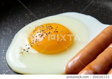 煎鍋裡煎蛋(加粗磨黑胡椒)和維也納香腸的烹飪場景。 煎鍋裡煎蛋(加粗磨黑胡椒)和維也納香腸的烹飪場景。 108182115