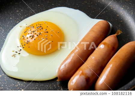 煎鍋裡煎蛋（加粗磨黑胡椒）和維也納香腸的烹飪場景。 108182116