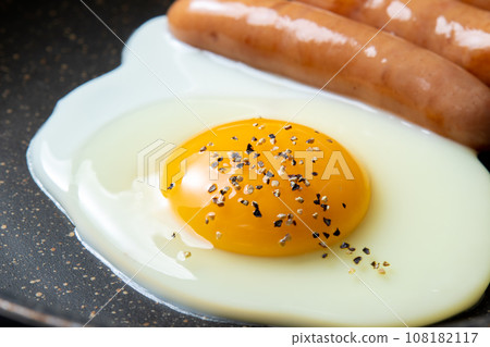 煎鍋裡煎蛋（加粗磨黑胡椒）和維也納香腸的烹飪場景。 108182117