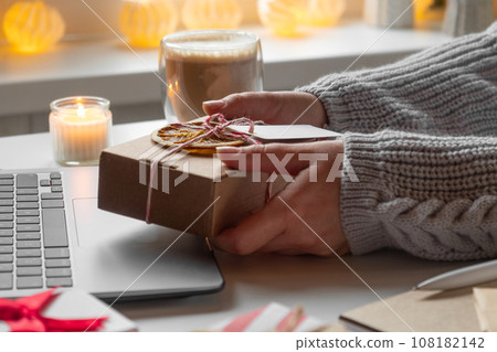 Female buyer makes order on laptop. Woman picking gifts online purchases at cozy home among gift boxes and packages. Winter sales, Black Friday. Christmas discount promotions. Blurred bokeh light. Female buyer makes order on laptop. Woman picking gifts online purchases at cozy home among gift boxes and packages. Winter sales, Black Friday. Christmas discount promotions. Blurred bokeh light. 108182142