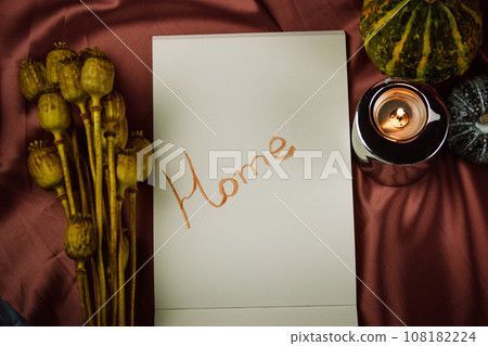 An open drawing and sketching notebook with white sheets and a word Home lies on a burgundy red silk sheet. Autumn decor for modern stylish interior, candles, pumpkins for Halloween top view, flatly. An open drawing and sketching notebook with white sheets and a word Home lies on a burgundy red silk sheet. Autumn decor for modern stylish interior, candles, pumpkins for Halloween top view, flatly. 108182224