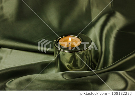 A candle in a metal holder on a dark olive green silk tablecloth. Stylish decor. 108182253